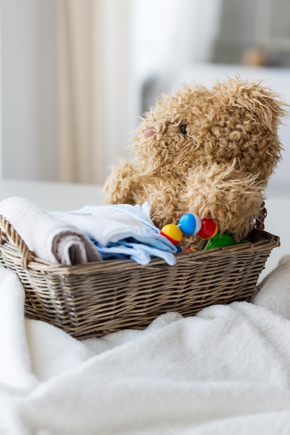 babyhood, motherhood, clothing and object concept - close up of baby clothes and toys for newborn boy in basket at home