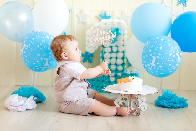 babyjongen 1 jaar in een fotostudio met een cake en ballonnen, verjaardag van een kind 1 jaar, baby eet cake