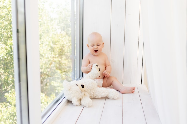 Babyjongen 8 maanden oud liggend in luiers op een wit bed met een fles melk thuis benen omhoog, bovenaanzicht, babyvoeding concept, baby drinkwater uit een fles