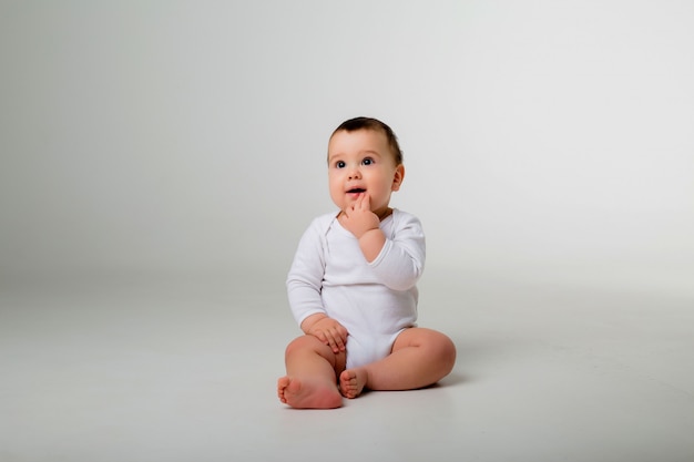 babyjongen 9 maanden in een witte Romper zittend op een witte muur
