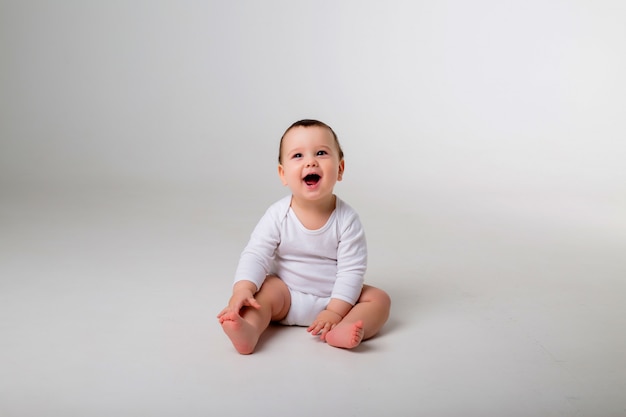 babyjongen 9 maanden in een witte Romper zittend op een witte muur