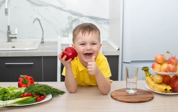 Babyjongen eet gezond voedsel door duimen omhoog gebaar te tonen. De kleine jongen eet graag groenten. het concept van gezond eten.
