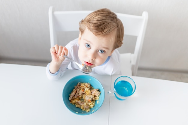 Babyjongen eet thuis met een lepel, het concept van voedsel en voeding voor kinderen.