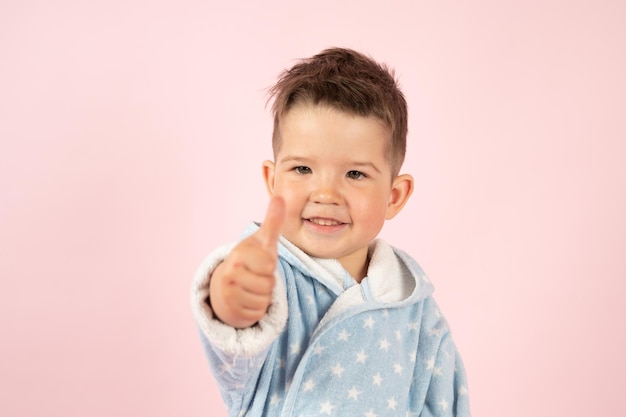 Babyjongen in blauwe badjas duimen omhoog op roze achtergrond Hoge kwaliteit foto