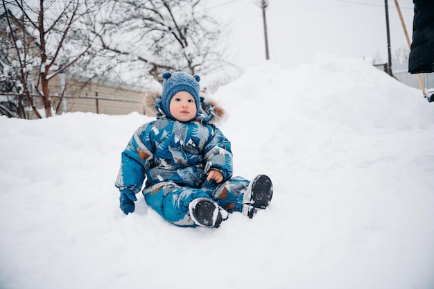 Babyjongen in blauwe overalls zittend op witte diepe sneeuw en genieten van mooie winterdag