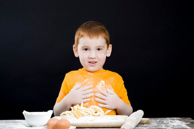 babyjongen in de keuken terwijl hij helpt met koken, mooie jongen met rood haar en mooie gelaatstrekken, baby speelt met bloem in de keuken en allemaal ingesmeerd met bloempoeder