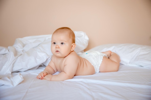 Babyjongen in een luier ligt op een wit laken, bedekt met een deken in de slaapkamer op het bed