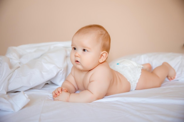 Babyjongen in een luier ligt op een wit laken, bedekt met een deken in de slaapkamer op het bed