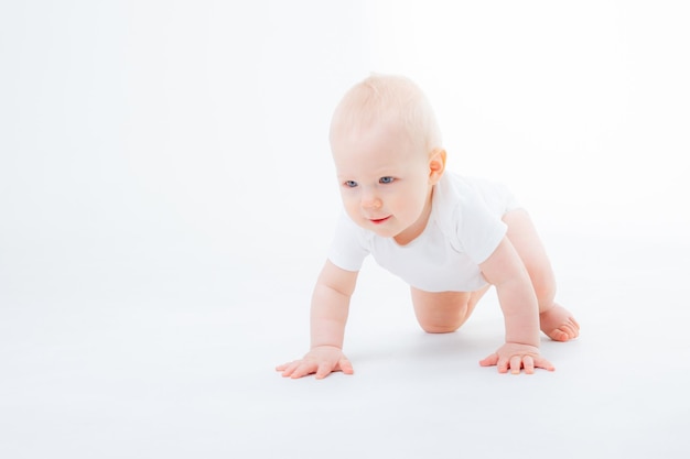 Babyjongen in een witte bodysuit die op een witte achtergrond kruipt