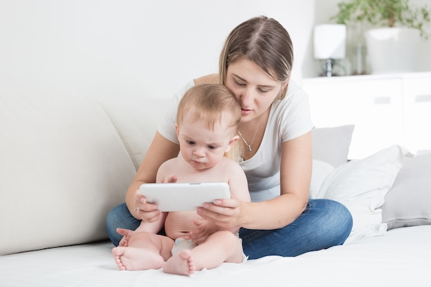 Babyjongen in luiers die tablet-pc gebruikt met zijn moeder