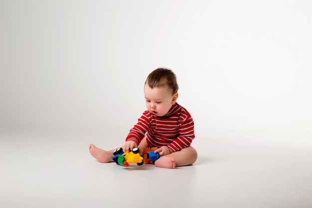 babyjongen in rode Romper zitten spelen met speelgoed op een witte muur