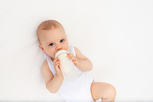 Babyjongen liggend op het bed in de kinderkamer op zijn rug en met een fles melk, de baby voeden, babyvoeding concept