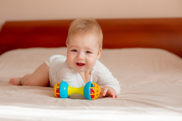 Babyjongen ligt op zijn buik met een stuk speelgoed op het bed in de slaapkamer