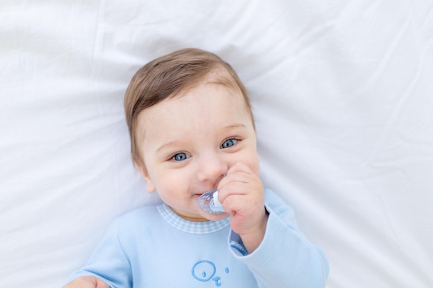 Babyjongen met fopspeen op bed voordat hij naar bed gaat in blauwe romper, gelukkige gezonde kleine baby