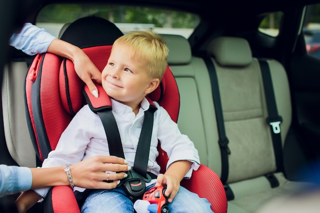 Babyjongen met krullend haar zitten in autostoeltje kind met speelgoedauto in handen