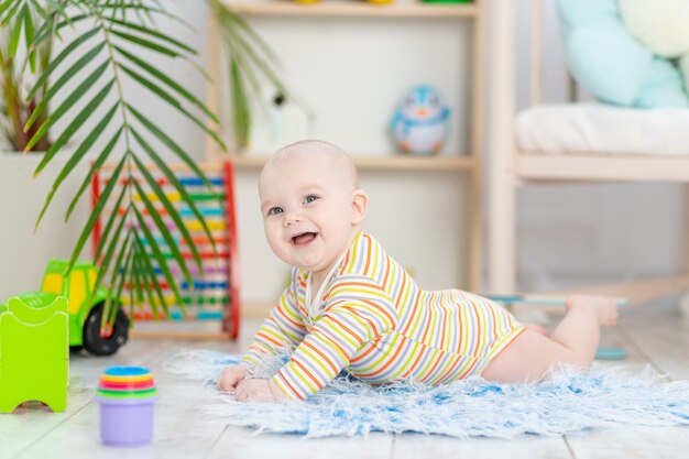 Babyjongen onder het speelgoed in de kinderkamer, schattige grappige lachende kleine baby die op de vloer speelt, het concept van de ontwikkeling van kinderen en spelletjes