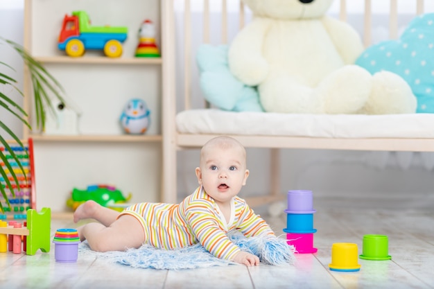 Babyjongen onder het speelgoed in de kinderkamer, schattige grappige lachende kleine baby spelen op de vloer, het concept van de ontwikkeling van kinderen en spelletjes