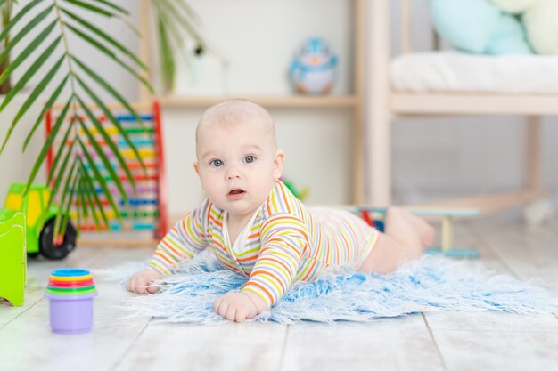 Babyjongen onder het speelgoed in de kinderkamer, schattige grappige lachende kleine baby spelen op de vloer, het concept van de ontwikkeling van kinderen en spelletjes