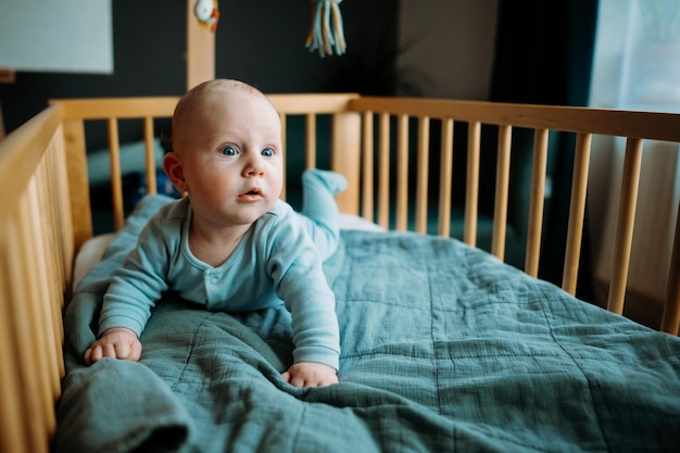 Babyjongen peuter kruipen in de wieg in de kinderkamer thuis kijken en glimlachen naar de camera