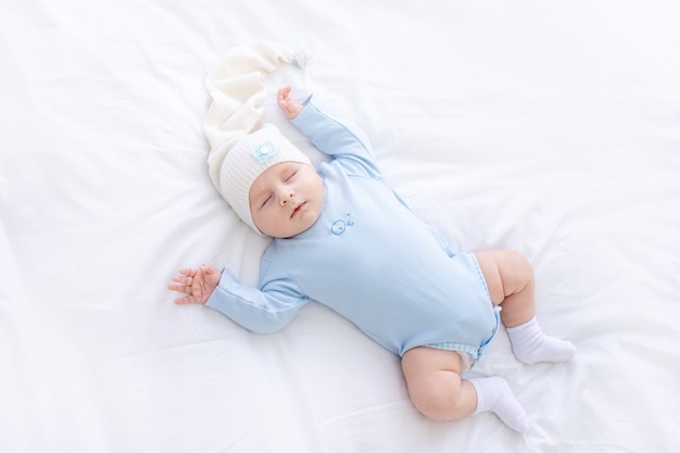 Babyjongen slaapt op het bed, liggend op zijn rug in blauwe pyjama's met zijn handen omhoog