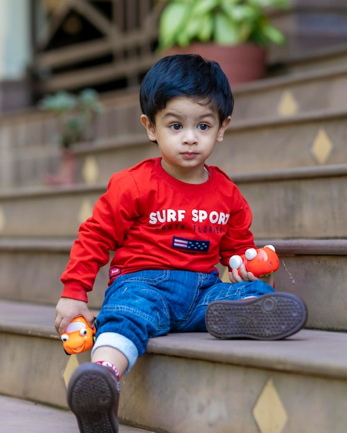 Babyjongen speelt met speelgoed dat op de trap zit en een rood t-shirt en een blauwe spijkerbroek draagt