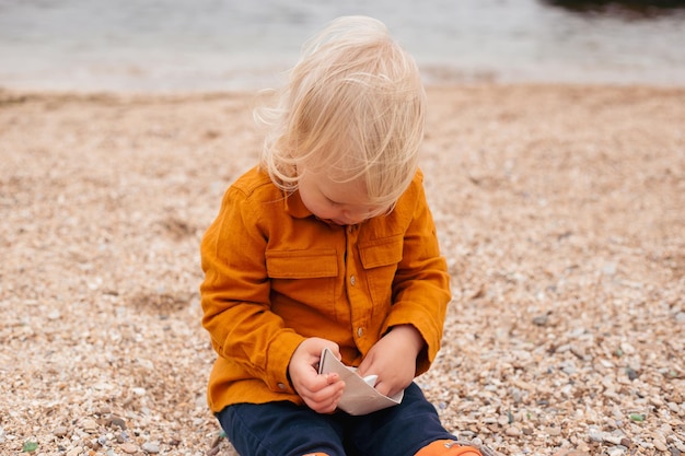 Foto babyjongen spelen met papieren bootje in het zand in de herfsttijd