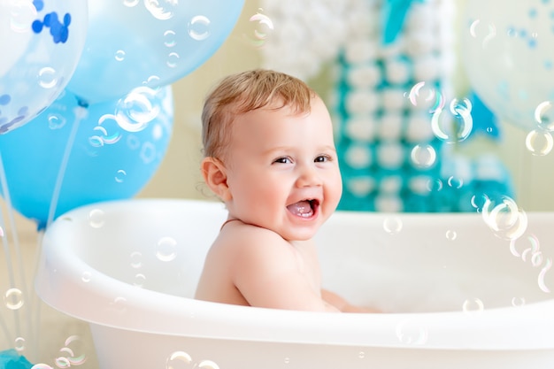 Babyjongen viert verjaardag 1 jaar in een bad met ballonnen, badende baby met blauwe ballonnen