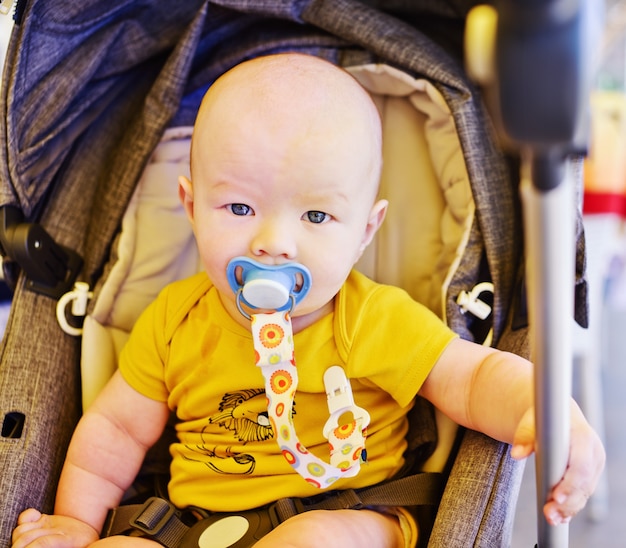 Babyjongen zit in de wandelwagen in de zomer