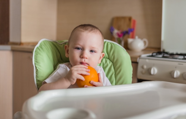 Babyjongen zit in een stoel en eet oranje