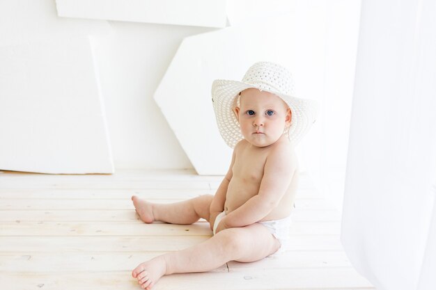 Babyjongen zit in luiers in een witte hoed