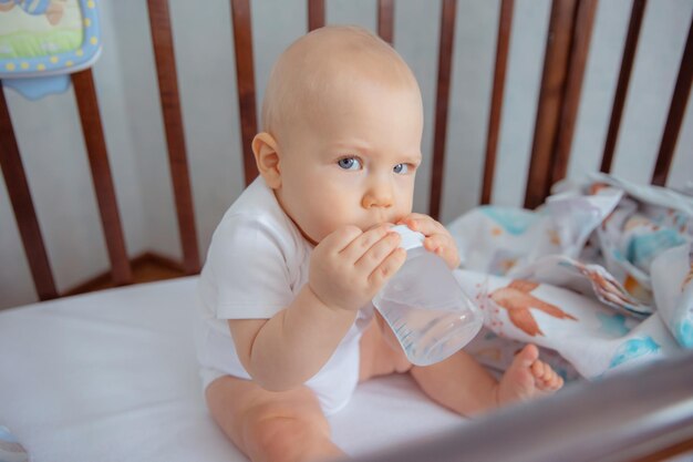 babyjongen zit op de wieg en drinkt water uit een fles