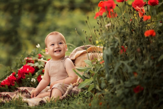 Babyjongen zit op het gras in de buurt van rode bloemen in de zomer poppy bloemen