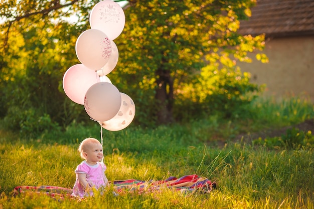 Babymeisje 1 jaar oud zittend op groen gras met roze en witte ballonnen in weide buiten close-up