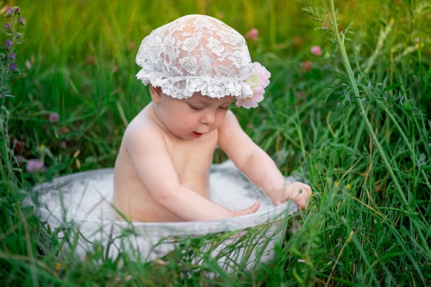 Babymeisje 10 maanden oud baadt in een bassin in het gras in de zomer.