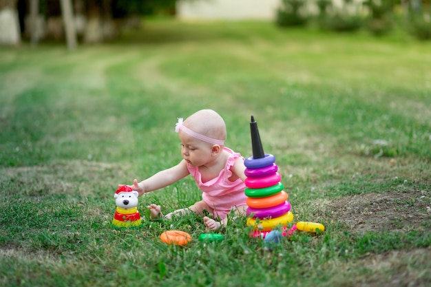 Babymeisje 10 maanden oud zittend op het gras in de zomer en spelen piramide
