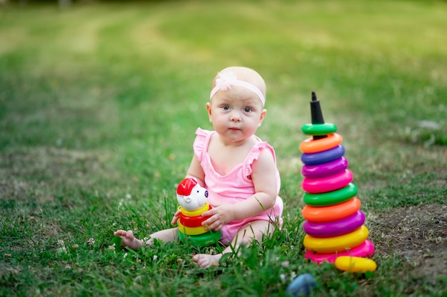 Babymeisje 10 maanden oud zittend op het gras in de zomer en spelen piramide