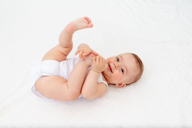 Babymeisje 6 maanden oud liggend in een wieg in de kinderkamer op haar rug en houdt haar benen, l, baby's ochtend, babyproducten concept