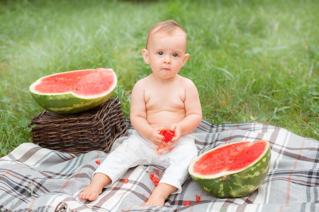 Babymeisje eet watermeloen in de zomer zittend op het gazon buiten