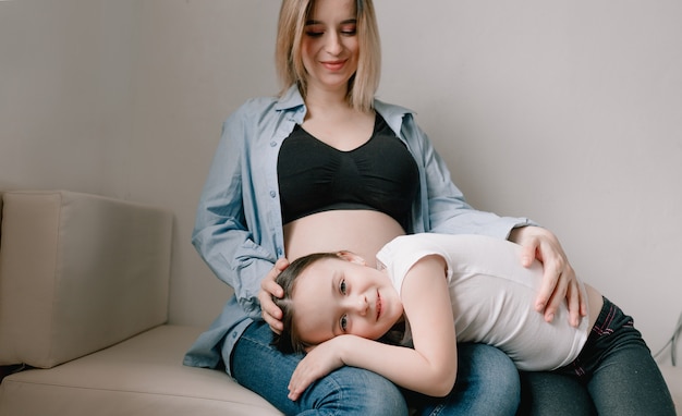 Babymeisje en zwangere moeder liefdevolle zusje naast moeders buik. gelukkig gezin