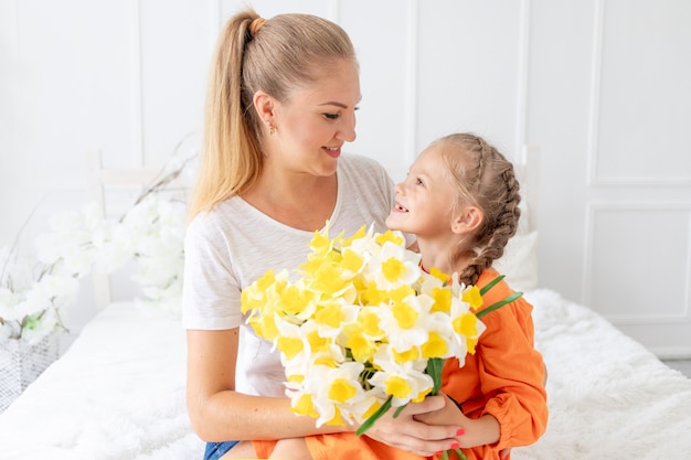 Babymeisje geeft bloemen aan haar moeder voor een vakantie op het bed thuis, het concept van liefde en moederschap of moederdag