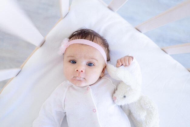 Babymeisje glimlachend op het bed op een wit katoenen bed met speelgoed dat in slaap valt of 's ochtends wakker wordt schattige kleine baby thuis blij en lachend