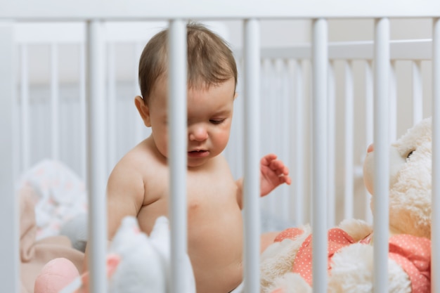 Babymeisje het spelen met een teddybeer in een wieg.