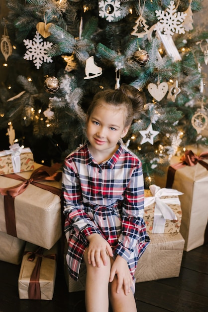 Babymeisje in de zitting van de plaidkleding dichtbij Kerstboom in giften