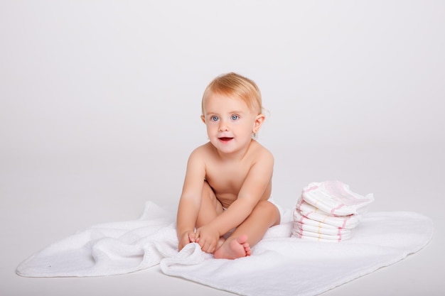 babymeisje in een luier met een stapel luiers op een witte achtergrond