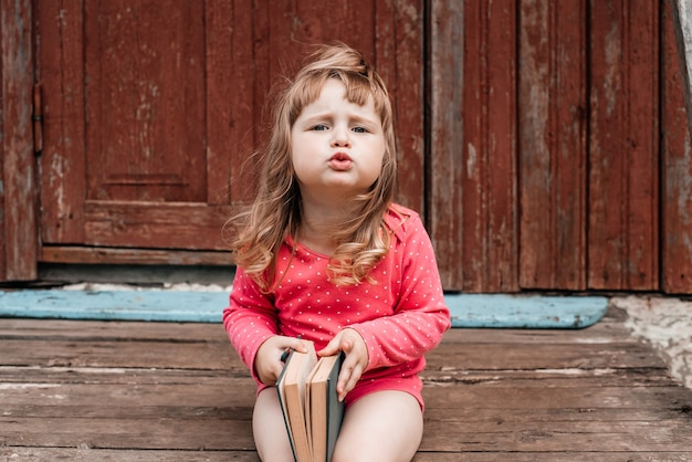 Babymeisje in een rood op groen gras en het lezen van een boek op een zonnige zomerdag.