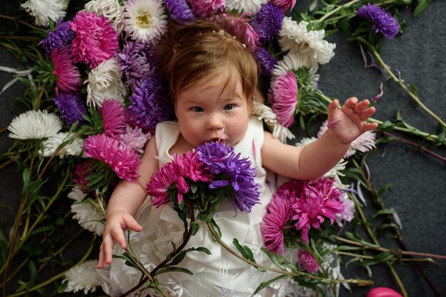 Babymeisje in het witte kleding spelen met bos van bloemen