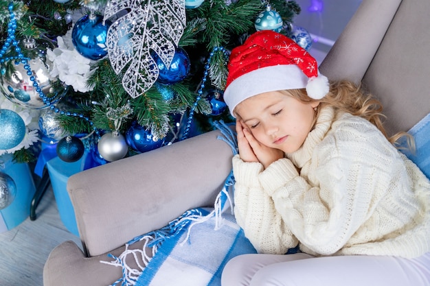 Babymeisje in kerstmuts slapen in de buurt van de kerstboom