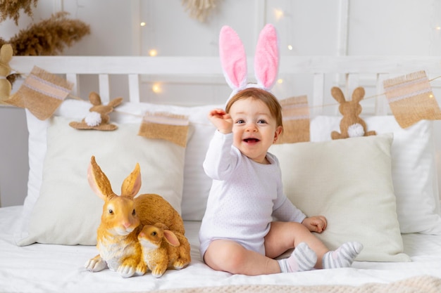 Babymeisje in konijnenoren op het bed thuis met beschilderde eieren en konijn Pasen concept schattige paasbaby wacht op de vakantie en verheugt zich