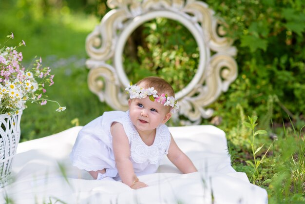 Babymeisje in witte kleding in een de lentetuin met bloemen