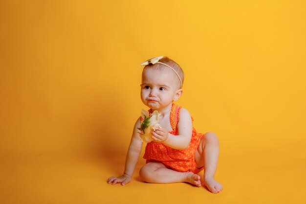 Babymeisje kruipt op een gele achtergrond met een bloem